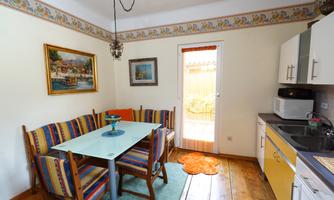 A bright kitchen with a table and colorful chairs. The room has a windowed porch with a view outside.