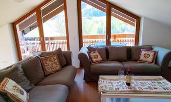 A cozy living room with modern sofas and large windows. The view overlooks a green mountain landscape.