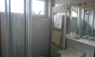 A modern bathroom with a shower cabin, a sink, and a large mirror. The walls are tiled, and there is a window that lets in daylight.