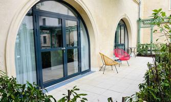 A modern terrace with large French doors and two stylish chairs. Surrounded by green plants, it gives an inviting impression.