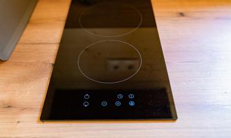 A modern cooking plate on a wooden countertop. The surface is black and has simple control knobs.