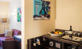 A stylish hotel room with a cozy seating area and modern artworks on the wall. Fresh fruit and drinks are ready on the table.