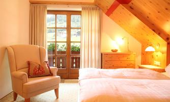 A cozy bedroom with a comfortable armchair and a large window. The room has wooden elements and is designed to be bright and inviting.