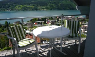A beautiful balcony overlooking a lake and the surrounding mountains. The table and chairs are modern and inviting.
