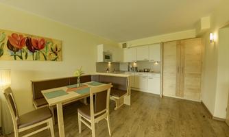A modern kitchen with a dining table and chairs. A colorful flower picture hangs on the wall.