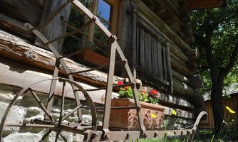An old metal machine stands in front of a wooden cabin. It is decorated with flower boxes and red flowers.