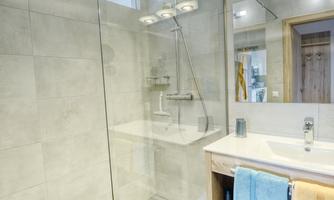 A modern bathroom with a walk-in glass shower and an elegant sink. The walls are brightly and minimally designed.