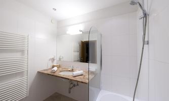 A modern bathroom with bright tiles and an elegant sink. The shower corner is equipped with a glass privacy screen.