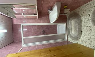 A small bathroom with pink tiles and a shower. There is a sink, a mirror, and a wooden cabinet.