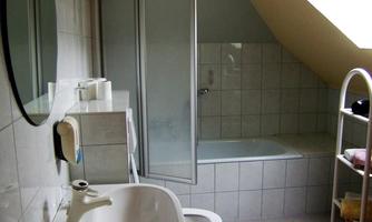 A modern bathroom with a bathtub, a shower, and a sink. The walls are tiled with light tiles.