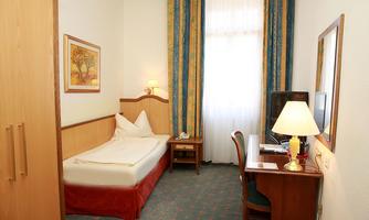 A single room with a bed, desk, and chair. The walls are light-colored and the curtains are colorful.