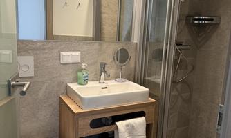 A modern bathroom with a shower and a wooden sink. The walls and the floor are in neutral shades of gray.