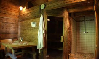 A cozy wellness area with wood paneling and soft light sources. The room features a sauna, a shower, and a table with chairs.