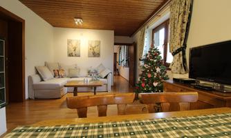 A cozy living room with a sofa and a table. A decorated Christmas tree stands in the corner.