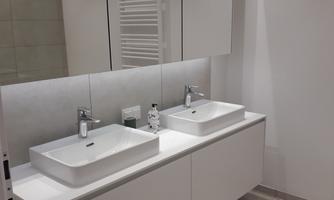 A modern bathroom with two sinks and a large mirror. The walls are bright and the decor is stylish and minimalist.