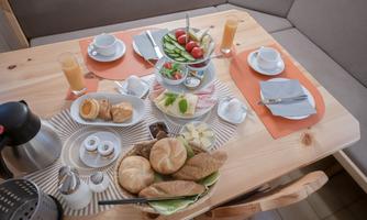 A beautifully set table with a variety of breakfast options, including rolls, fruit salad, and drinks. The atmosphere feels inviting and cozy.