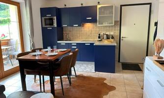 A modern kitchen with blue cabinets and a cozy dining nook. The room is bright and inviting, featuring a wooden dining area.