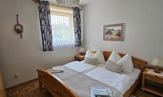 A cozy bedroom with a double bed and two nightstands. The room has bright walls and daylight streaming in through the window.