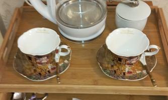 A tea service with two cups and saucers is on a tray. Next to a kettle are tea bags and a sugar container.