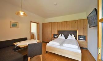 A cozy room with a double bed and a seating area. Wooden details and plenty of daylight create an inviting atmosphere.
