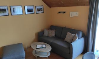 A modern living room with a gray sofa and a round table. Pictures hang on the wall and there is a large curtain next to the window.