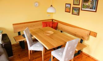 A cozy dining area with a wooden table and a bench. Pictures hang on the wall, and the walls are painted yellow.