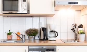 A modern kitchen with a microwave, a kettle, and a coffee machine. On the countertop, there are plants and kitchen utensils.