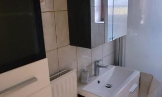 A modern bathroom with a simple sink and a mirror. Next to the sink is a shower area and cabinets for storage.