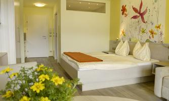 A bright and modern room with a double bed and a blooming wall design. On a table are yellow flowers that give the room a friendly atmosphere.