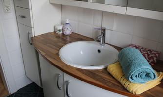 A modern bathroom with a round sink and wooden base. Two towels in fresh colors are ready.