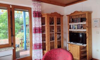 A cozy room with red armchairs and a television.  
Large windows provide plenty of light and a view of the greenery.