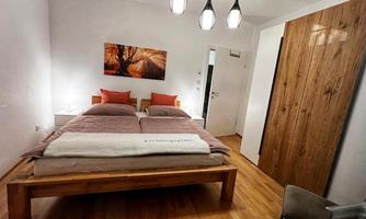 A modern bedroom with a large double bed and wood decor. On the wall hangs a painting with autumn colors.