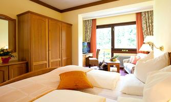 A cozy hotel room with a double bed and soft pillows. Large windows offer a view of a light-filled living area.
