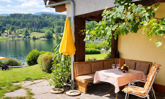 An inviting outdoor area with a table and cozy seating. In the background, you can see a picturesque lake and green landscapes.