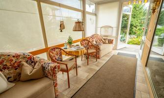 A cozy conservatory with comfortable furniture and a table. Large windows provide a view of the garden.