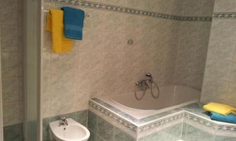 A bathroom with a bathtub and a shower. Colorful towels are lying on the bathtub and the shower.