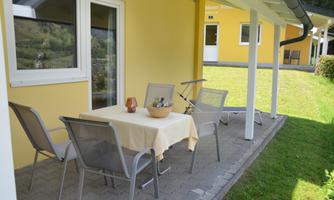 A cozy patio with a table and six chairs. The wall is painted in a light yellow and there is a green lawn in the background.