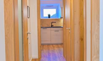 A bright hallway with wooden doors and a modern kitchen unit at the end. The floor is made of wood and the light creates an inviting atmosphere.