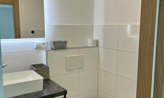 A modern bathroom with white tiles and a gray vanity. The decor is simple and functional, featuring a large mirror and a clean design.
