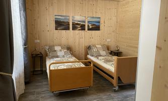 A cozy room with two single beds and wooden paneling. Pictures of landscapes hang on the wall.