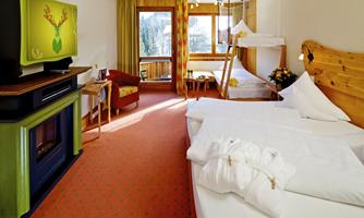 A cozy hotel room with two beds and a television. Large windows provide plenty of light and offer a view of nature.