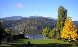 A picturesque landscape by the lake with colorful autumn trees. In the background, mountains rise under a clear blue sky.
