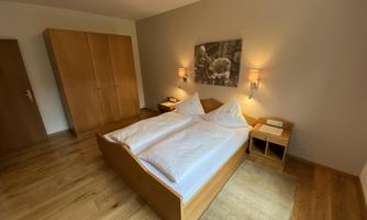 A cozy bedroom with a double bed and wooden cabinets. Soft lighting and a carpet create a warm atmosphere.