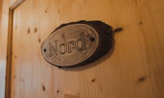 An invisible sign with the inscription "North" on a wooden wall. The sign is oval and made of natural wood.