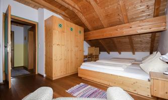 A cozy room in the attic with wooden ceilings and two single beds. There is a wooden wardrobe and a small rug on the floor.
