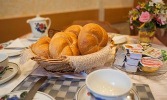 A basket of fresh rolls is on the table. Next to it are a cup and small portions of spreads arranged.