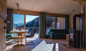 A modern living and dining room with large windows and a view of the mountains. The furnishings are made of wood and provide a cozy atmosphere.
