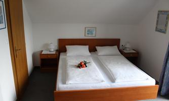 A cozy bedroom with two single beds and minimalist furniture. The decoration includes a small flower arrangement on one of the beds.
