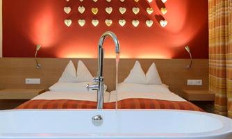 A modern bedroom with two beds and a freestanding bathtub in the foreground. Colorful heart-shaped lights hang on the wall, creating a cozy atmosphere.