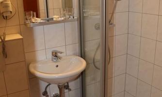 A small bathroom with a shower, sink, and mirror. The walls are tiled, and towels are provided.
